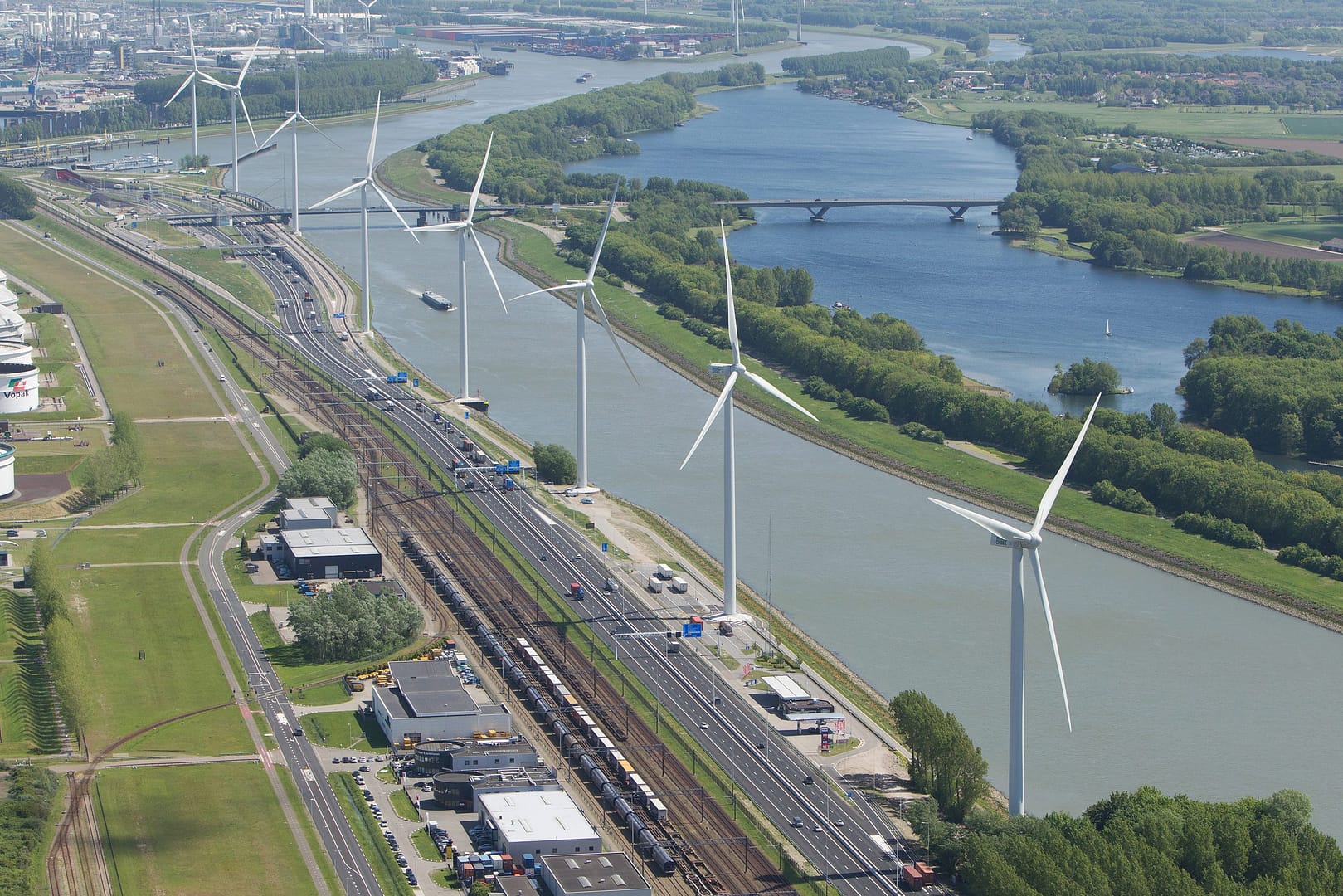 a wind farm next to a river and a train track.